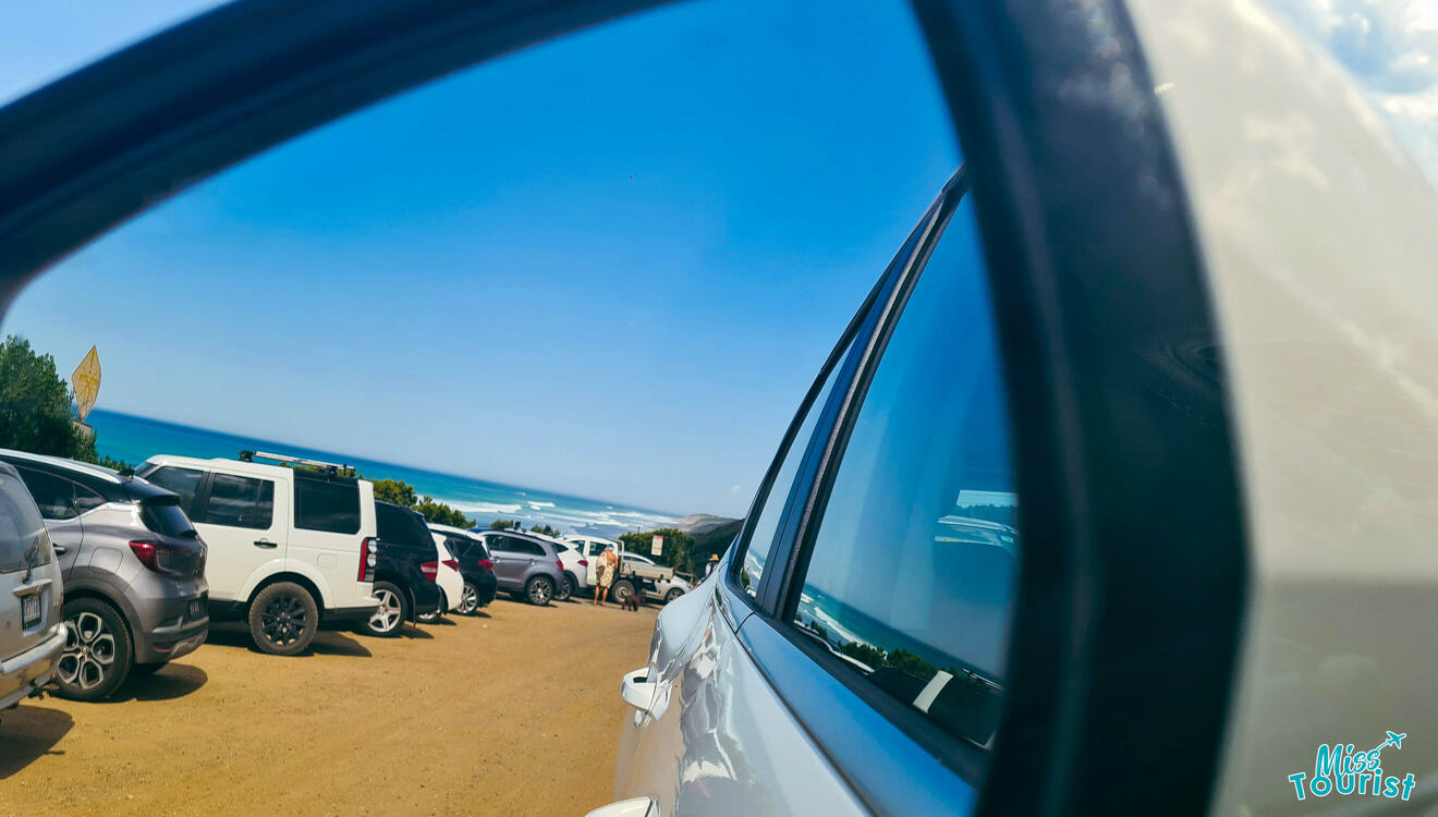 A car parked on a beach with a view of the ocean in the rear view mirror.