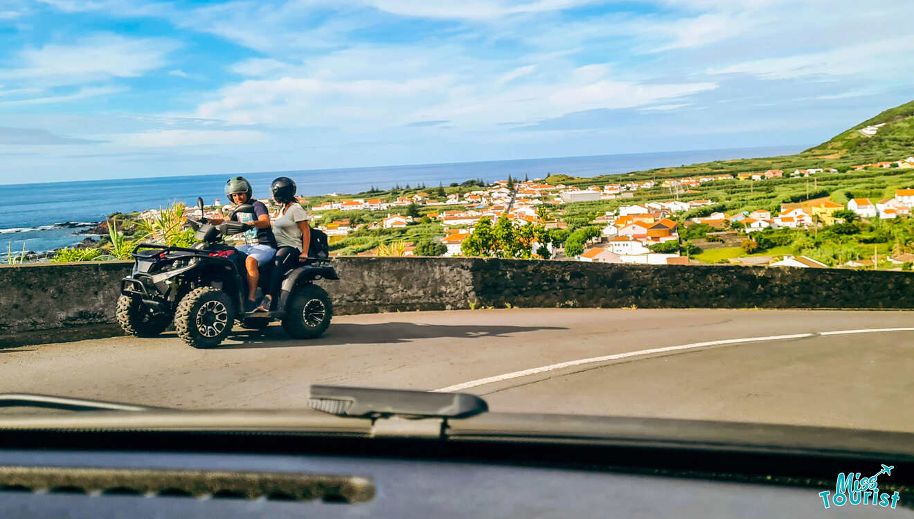 Two people riding atvs on a road with a view of the ocean.