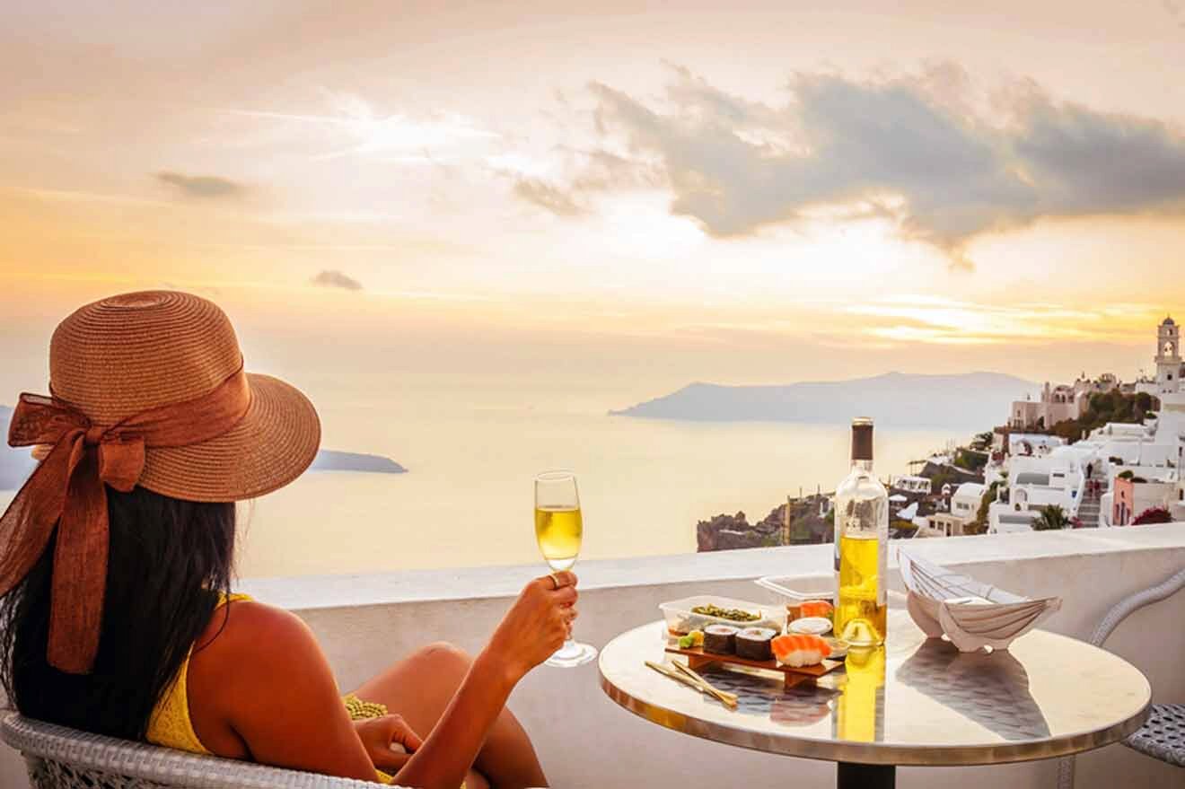 A woman sitting at a table with wine and food overlooking the sea.