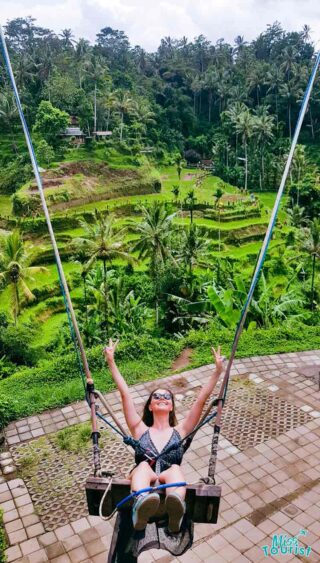 A woman is swinging on a swing in a rice field.