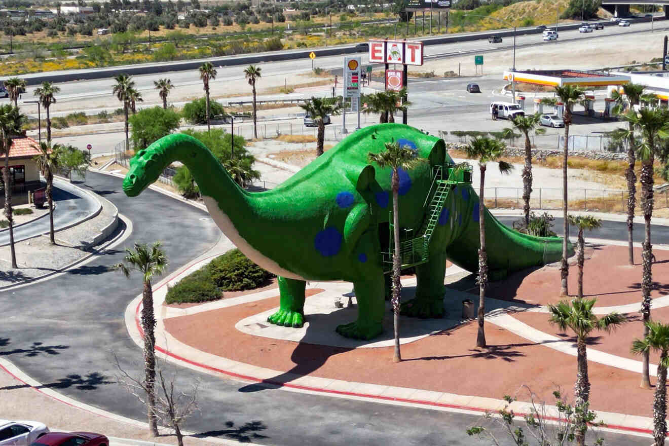 A green dinosaur sits in the middle of a parking lot.