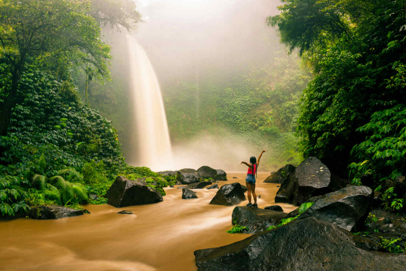A woman standing in front of a waterfall in the jungle.