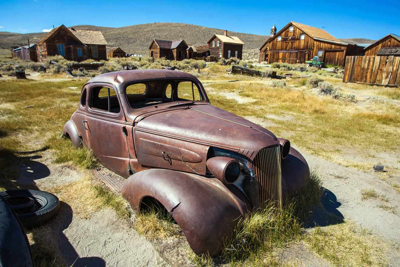An old rusted car sits in the middle of a ghost town.