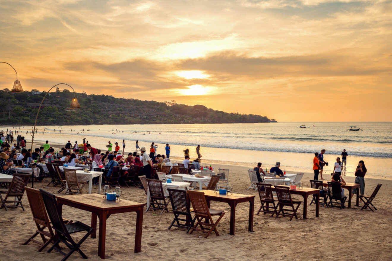 A group of people sitting at tables on the beach at sunset.