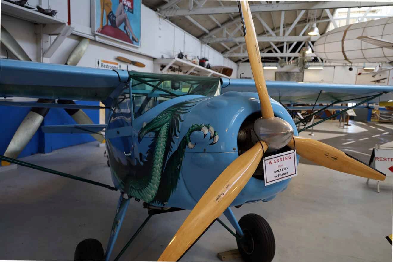 A blue biplane is on display in a museum.