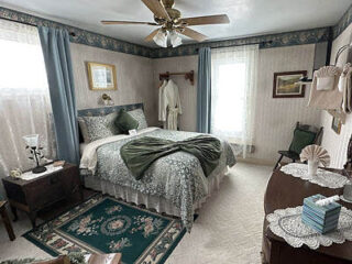 A bedroom with a bed, dresser, and a fan.