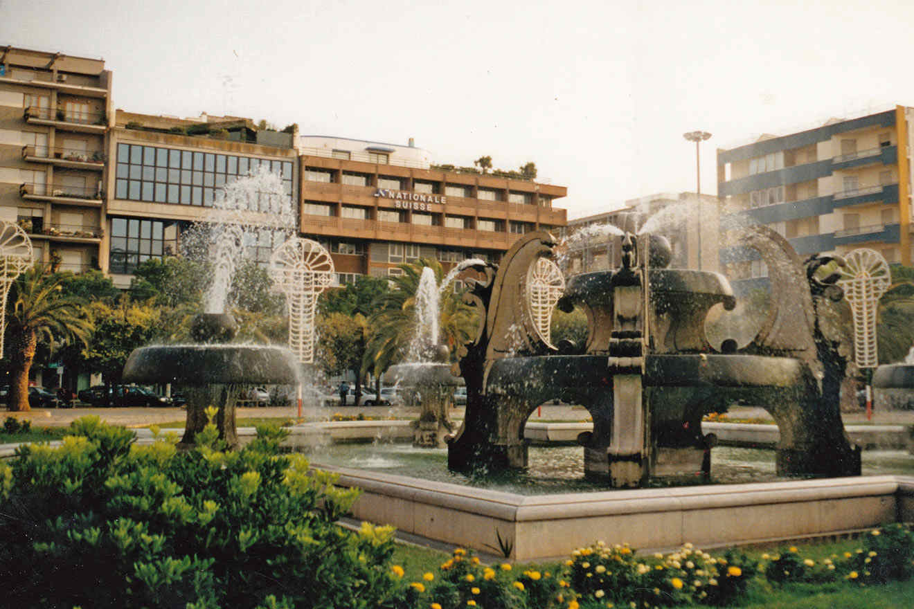 A fountain in front of a building surrounded by plants