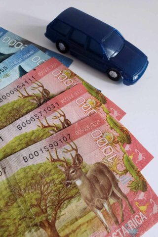 A toy blue car next to a stack of bank notes.