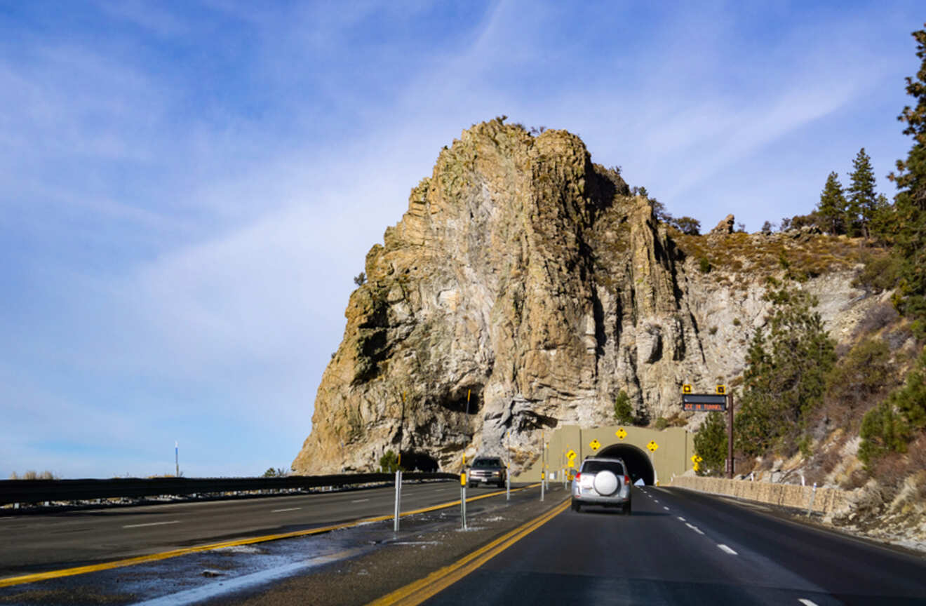 a car driving toward a tunnel in a cliff