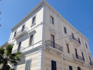 A white three-story building with balconies and tall windows under a clear blue sky.