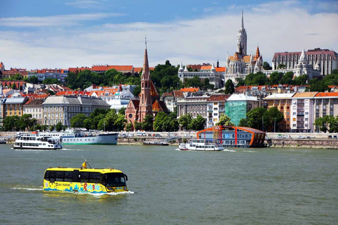 A yellow floating bus traveling down a river with a city in the background.