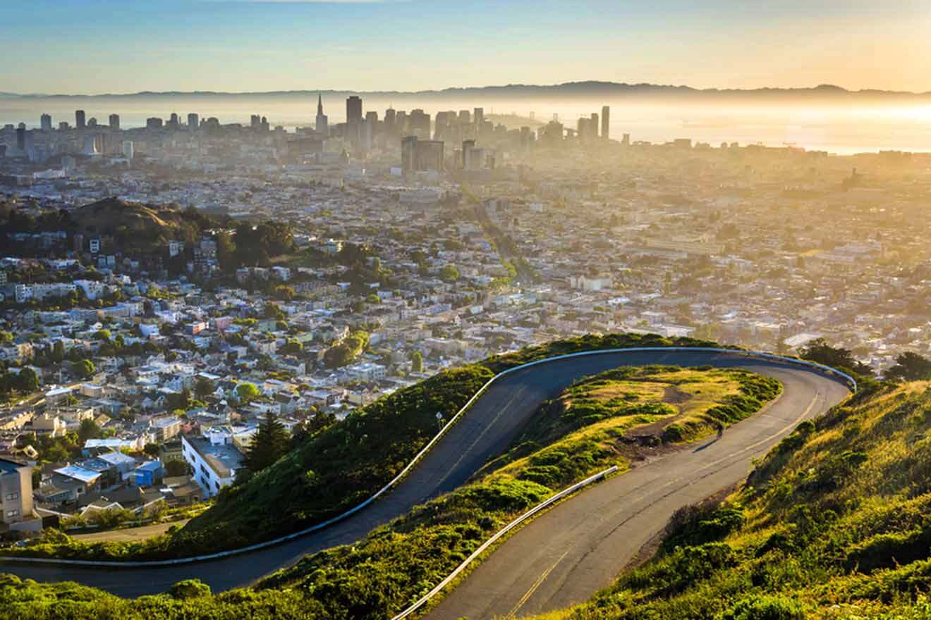 The city of san francisco is seen from the top of a hill with a curvy road in the foreground