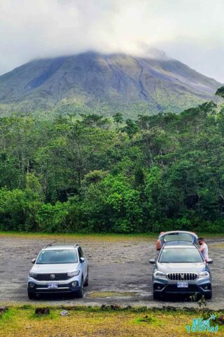 Three cars parked in front of a volcano.