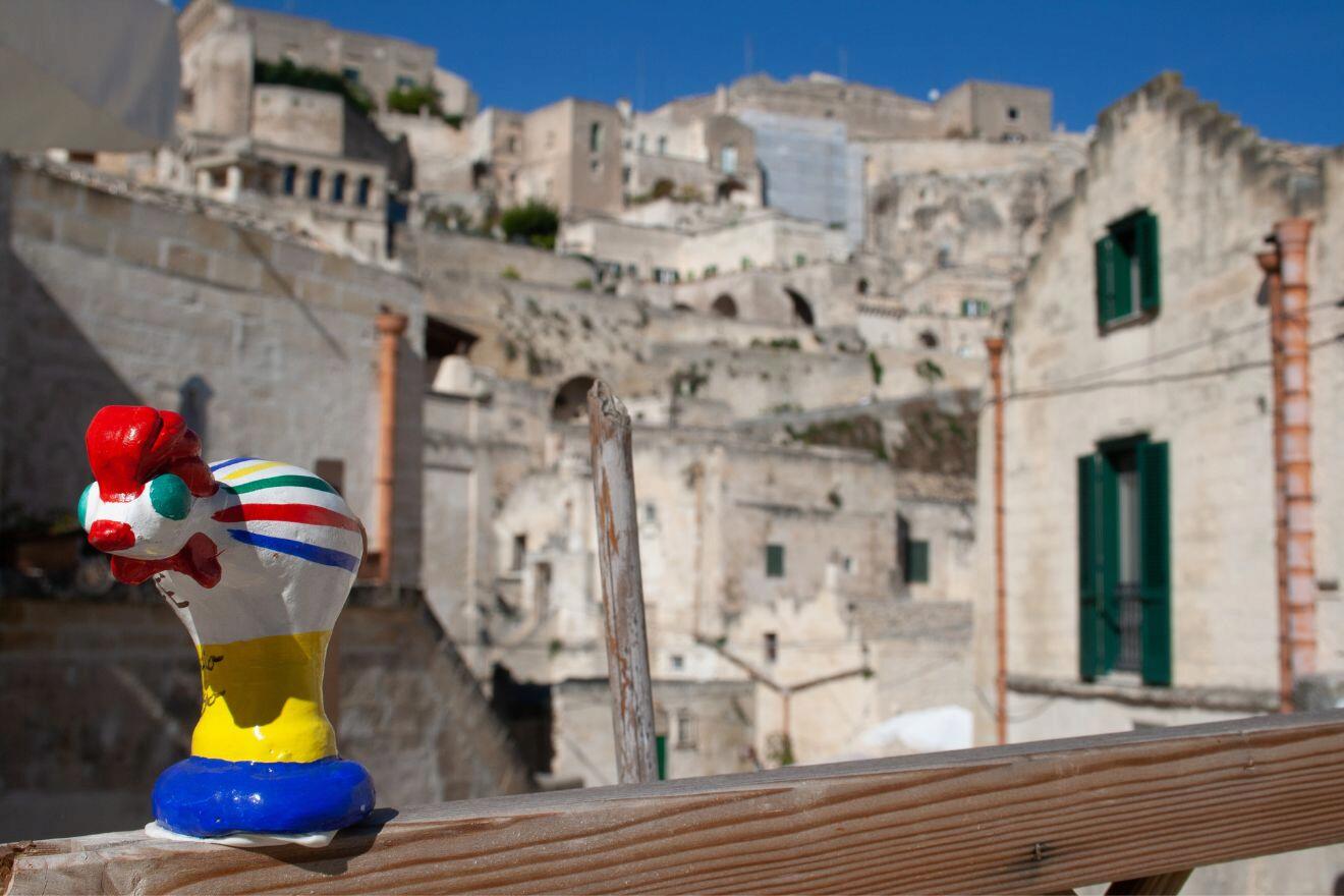 Small statue of colorful rooster sits on a wooden railing.