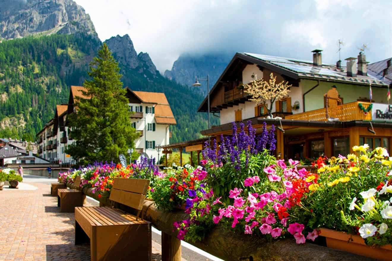 A bench with flowers in front of a mountain village.
