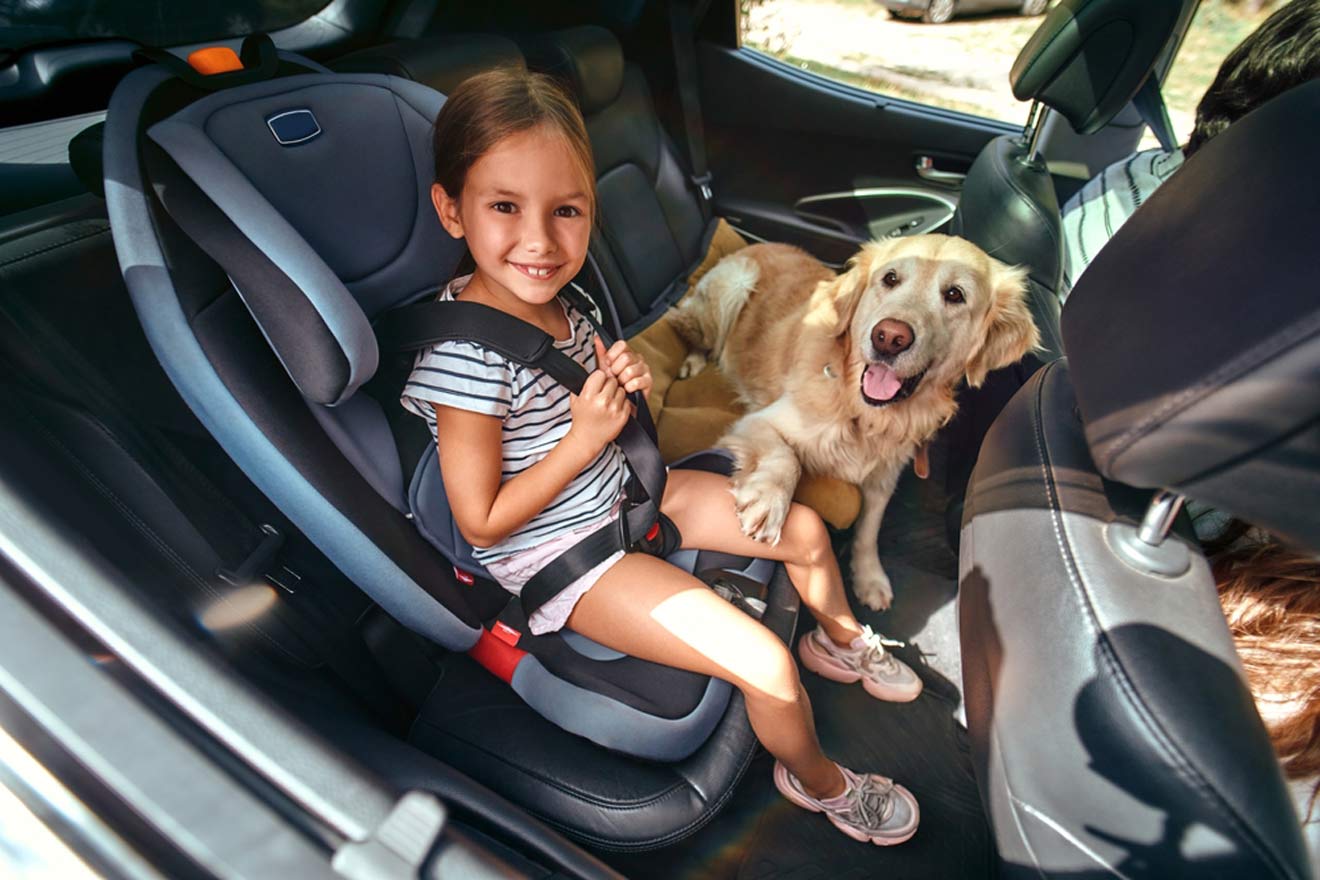 A girl sits in the back seat of a car with a dog.