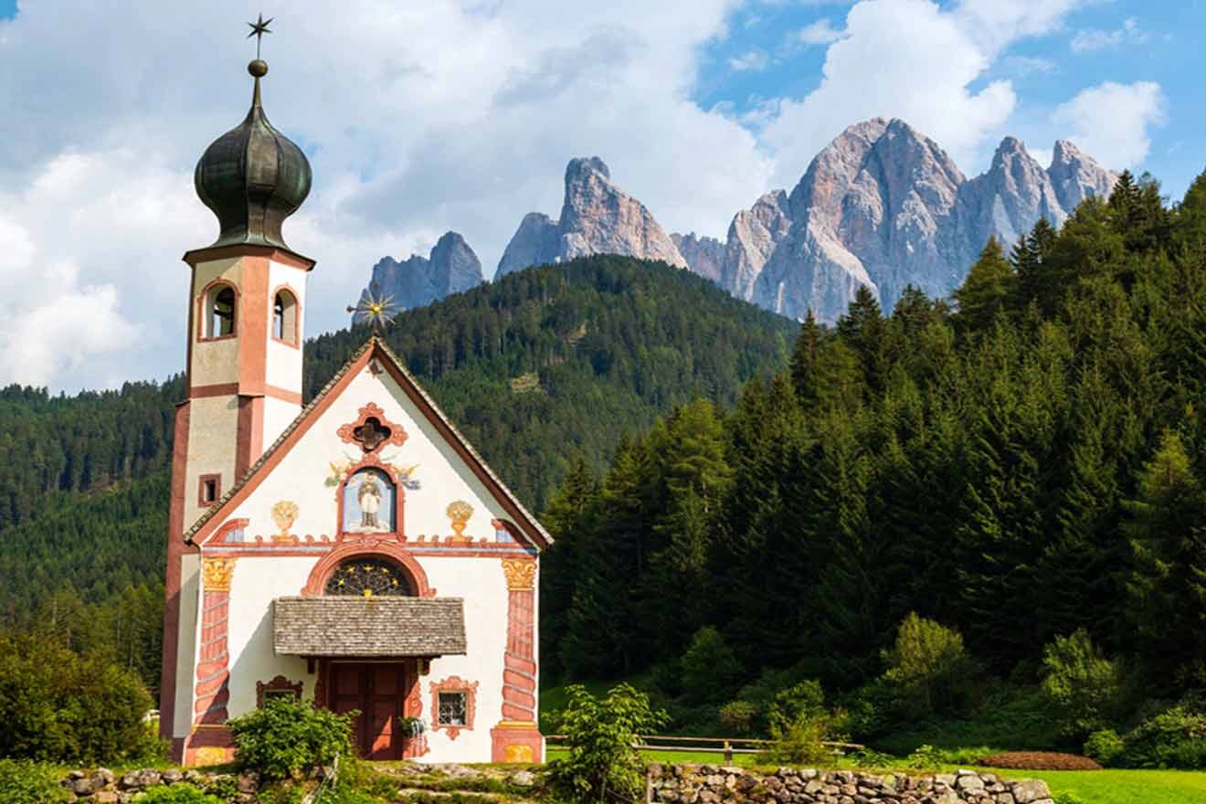 A church in the middle of a green field with mountains in the background.