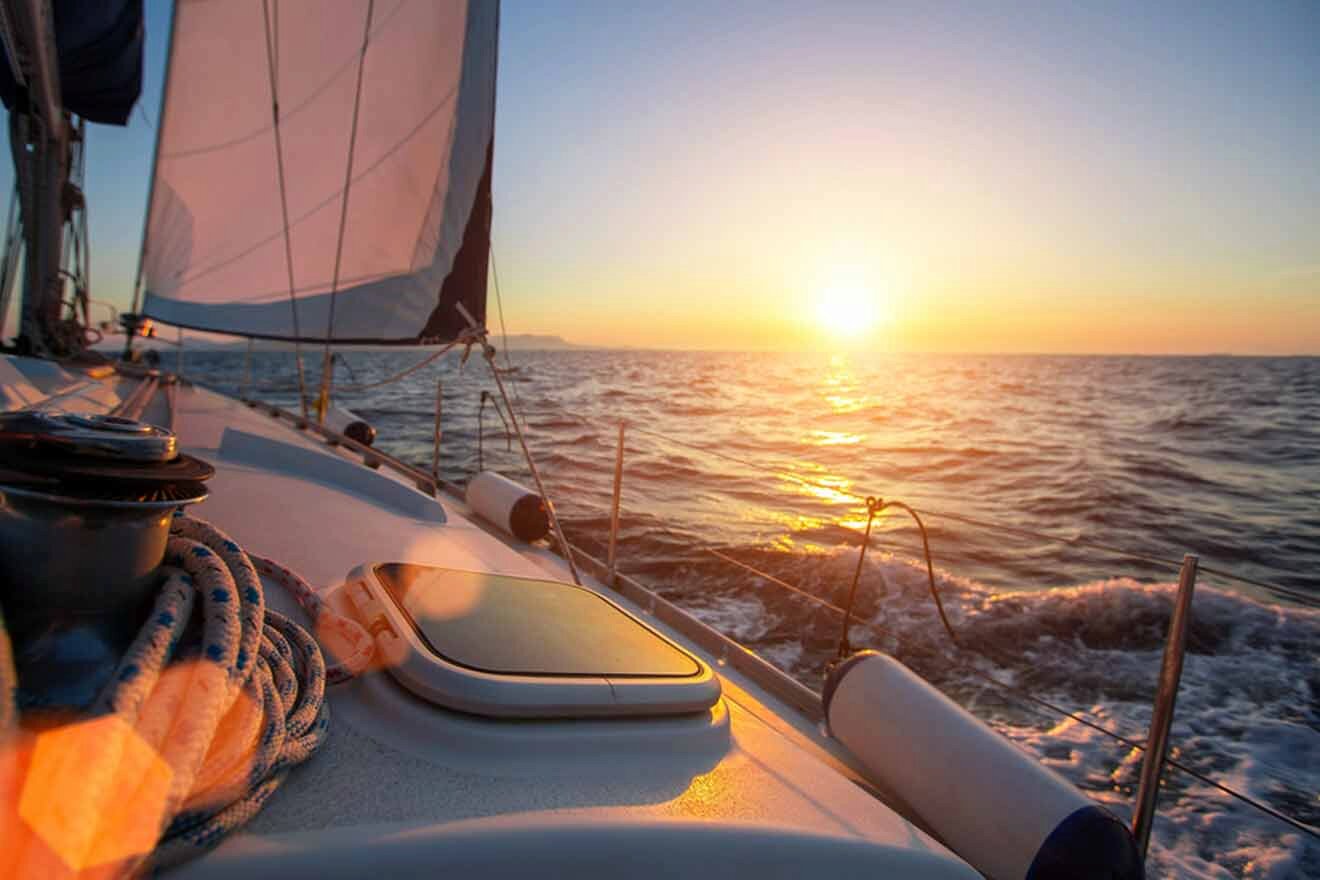 A sailboat in the ocean with the sun setting behind it.
