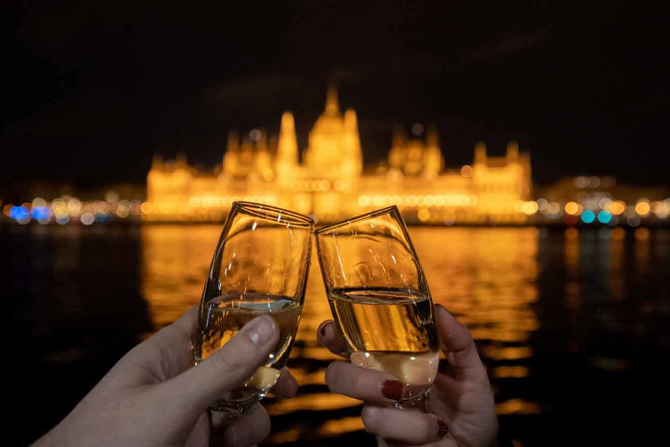 Two people toasting champagne in front of the hungarian parliament building.