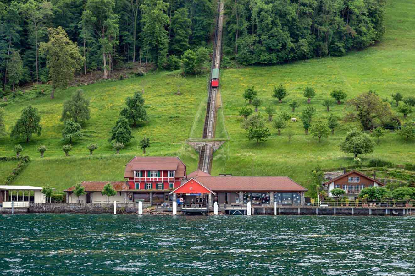 A red house on a hill next to a lake with a funicular train in the background