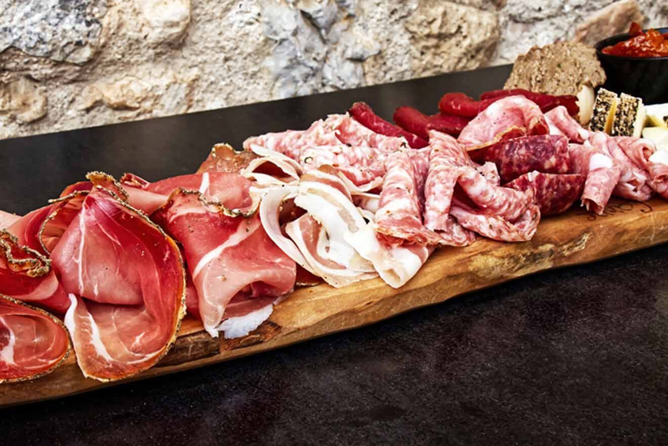 A wooden board with a variety of italian food on it.