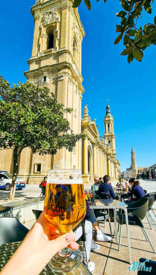 A person holding a glass of beer in front of a church.