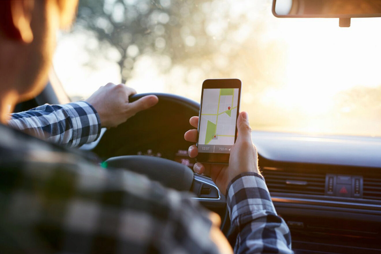 A man in a car holding a phone with gps while driving