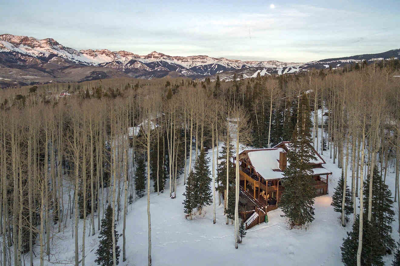 An aerial view of a cabin surrounded by snowy mountains.