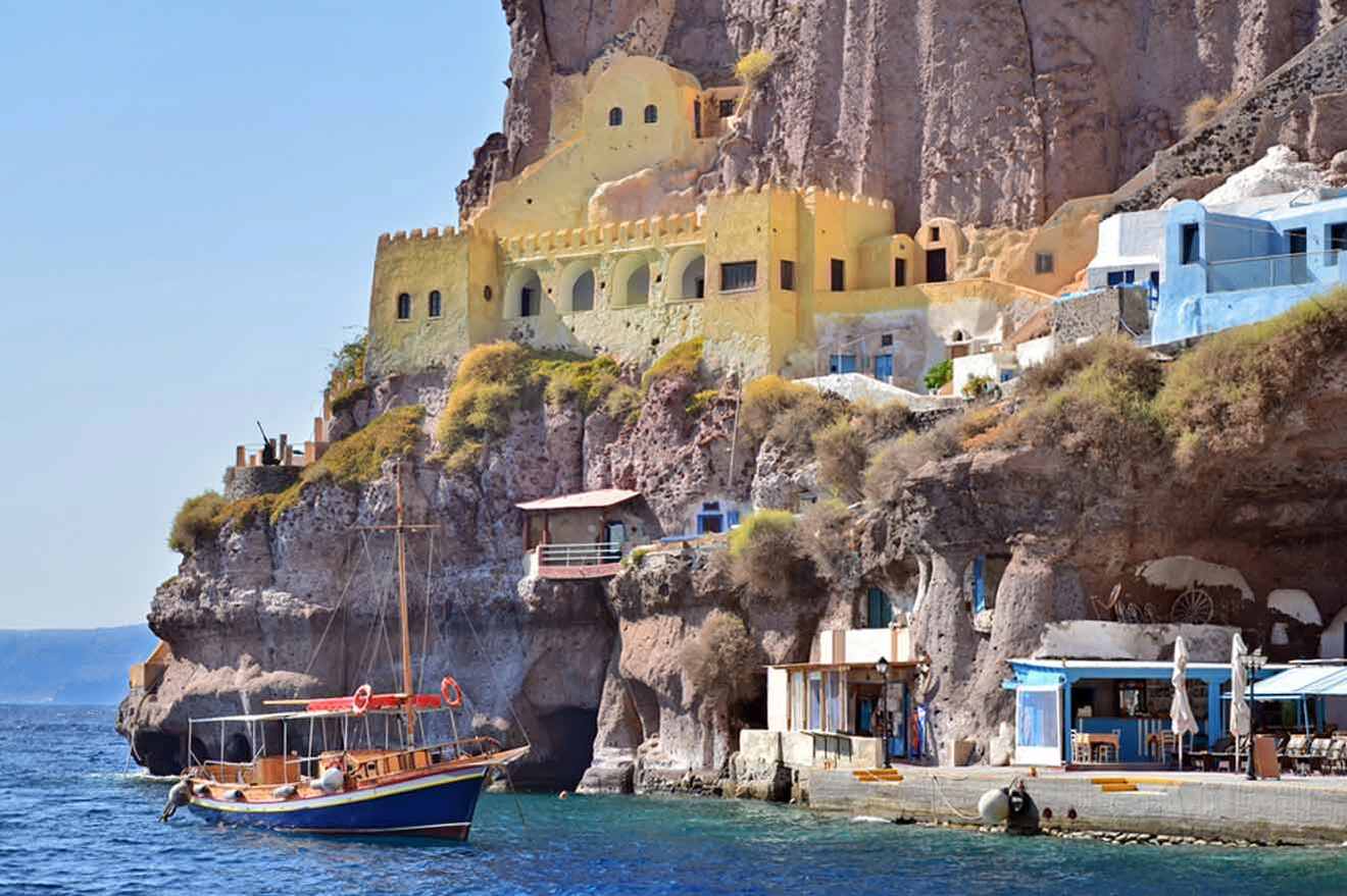 boat next to a tall rock with built in buildings