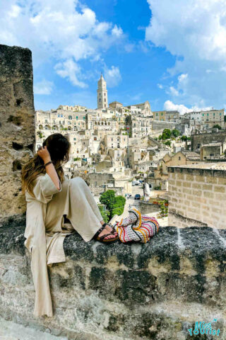 A woman sitting on a wall overlooking a city