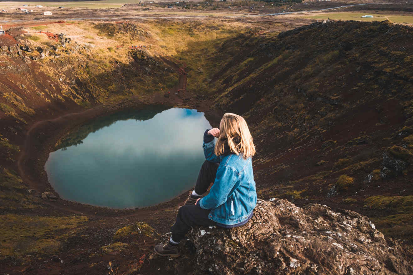 A woman sitting on top of a crater in iceland.