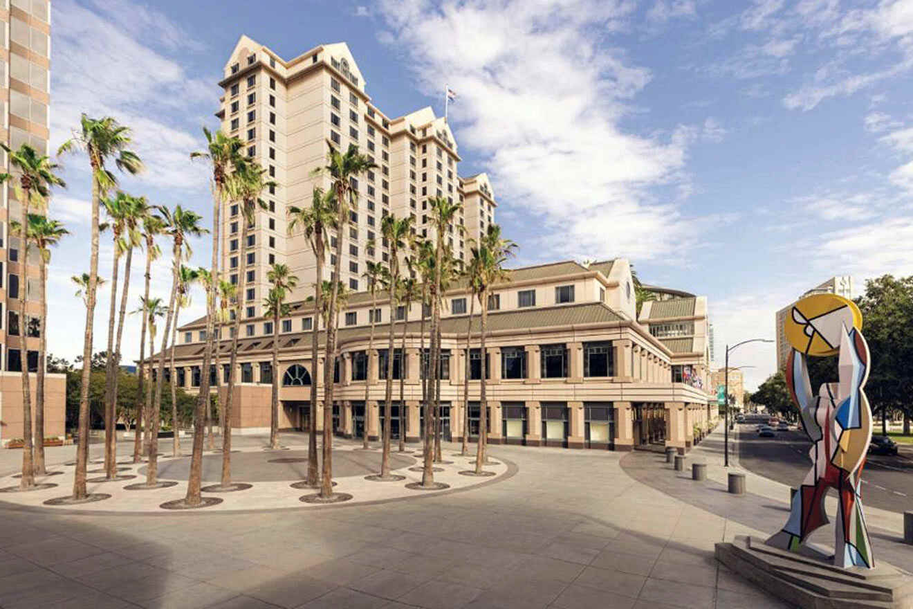 A large building with palm trees in front of it and an abstract statue