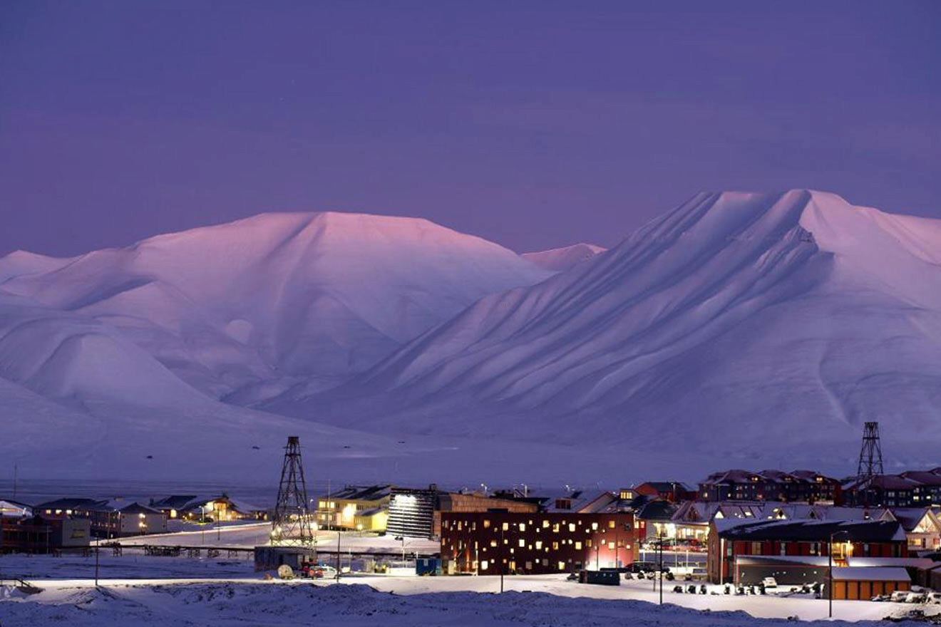 view of some buildings at night with mountains covered in snow.