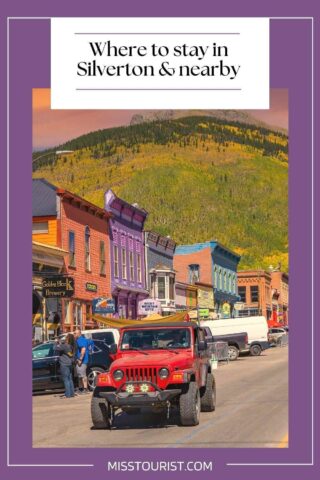 red jeep on a street with colourful buildings and parked cars with hill in the background