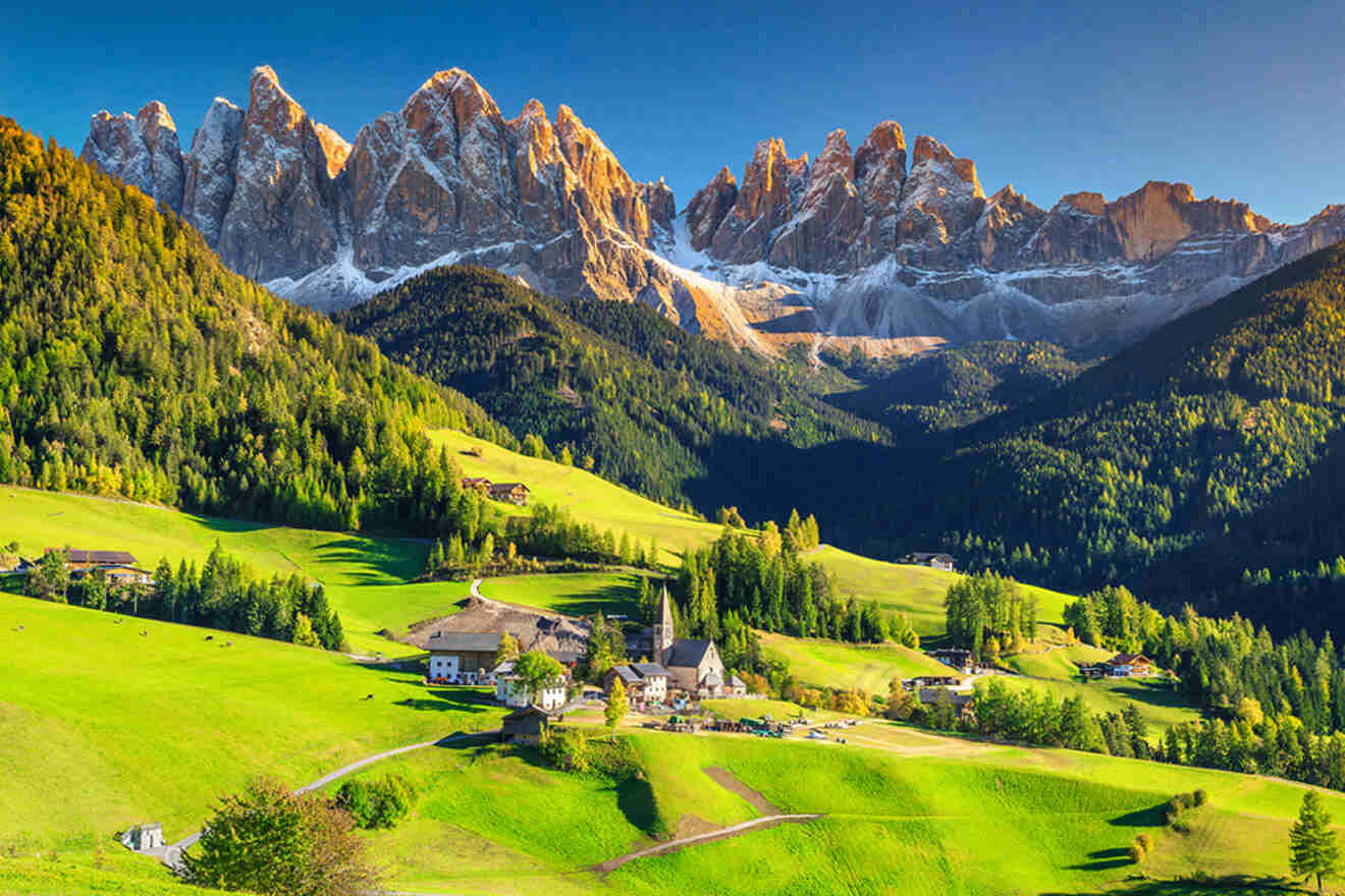 various houses on a green field with the dolomite mountains in the background.