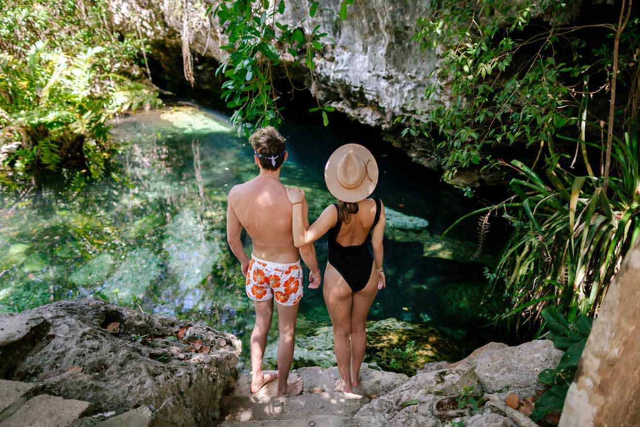 A man and woman standing next to a cenote in the jungle.