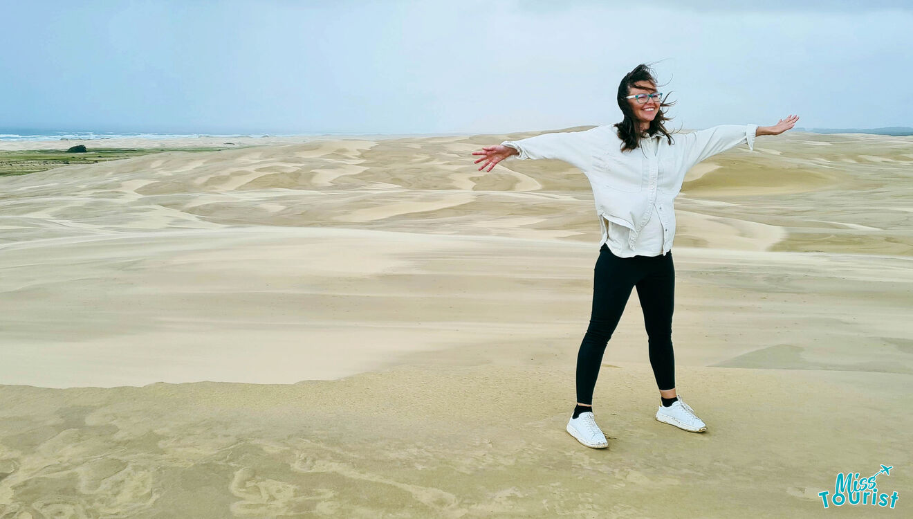A woman standing on a sand dune with her arms outstretched.