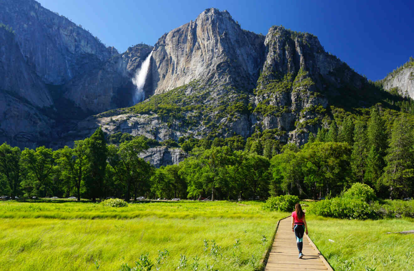 a girl walking on a wooden boardwalk towards rocky mountains