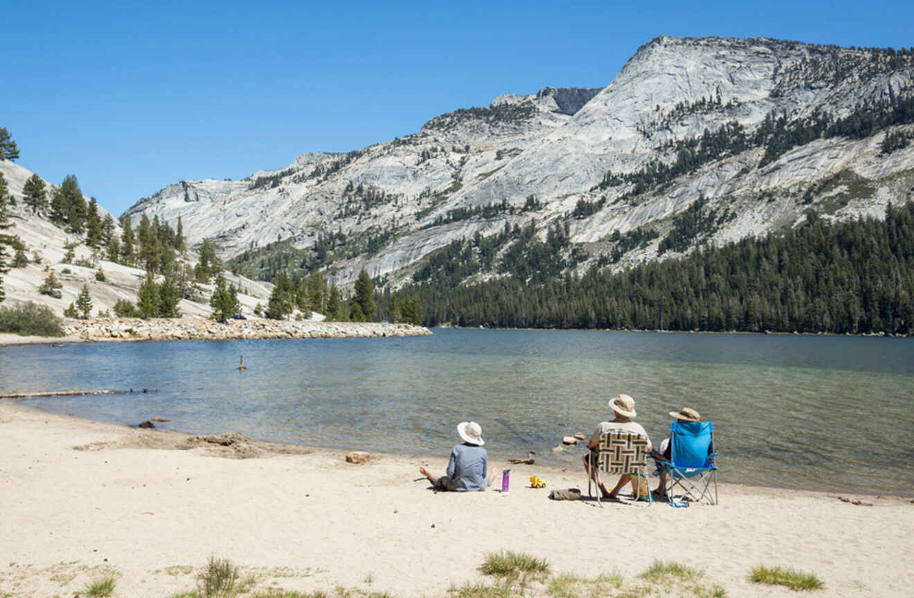 people sitting on chairs on a beach of a lake with rocky mountains in the background