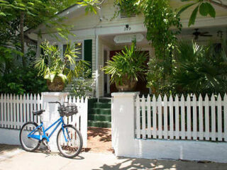 A blue bicycle is parked in front of a white picket fence.