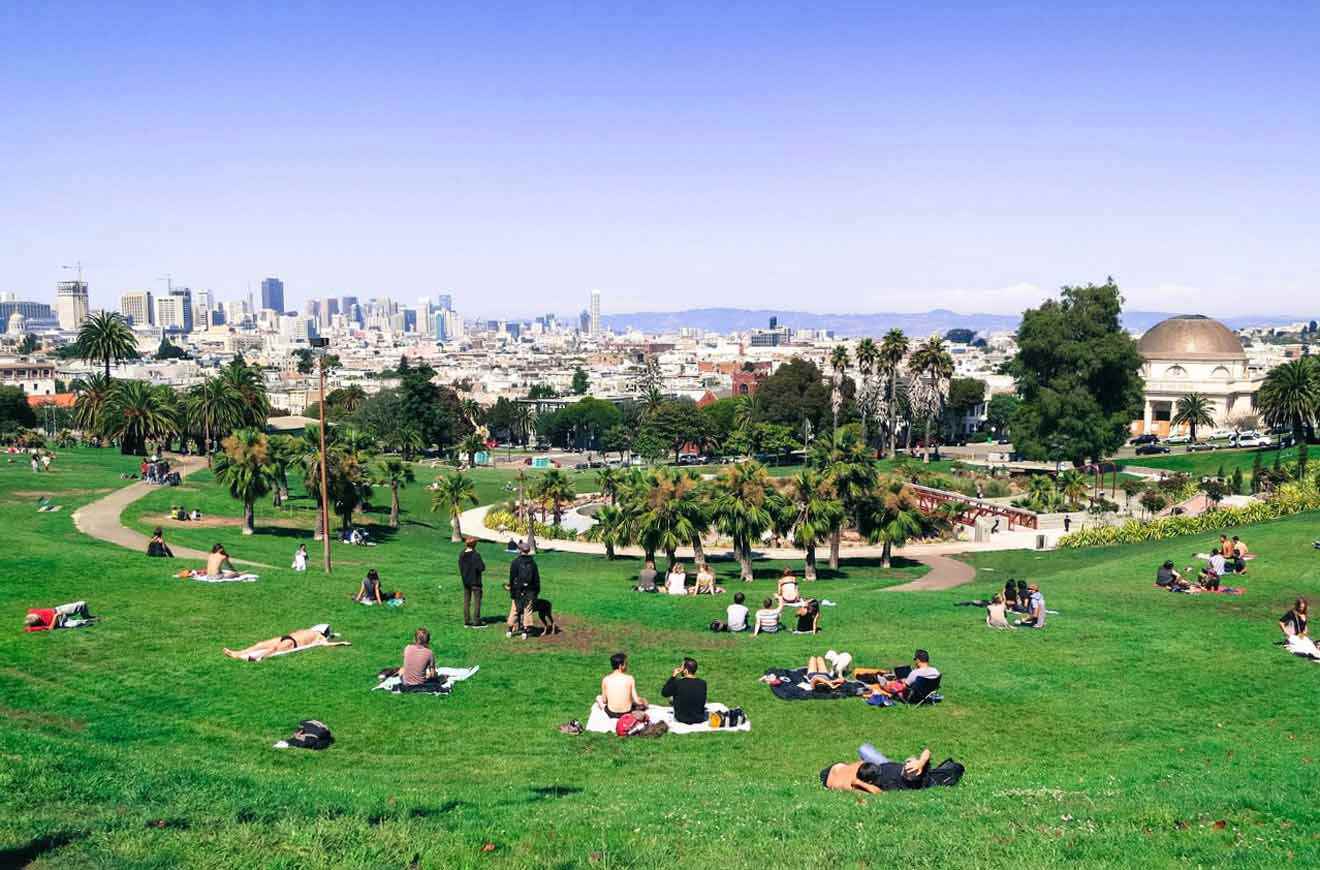 people enjoying a warm sunny day sitting on the grass in a park with a city in the background