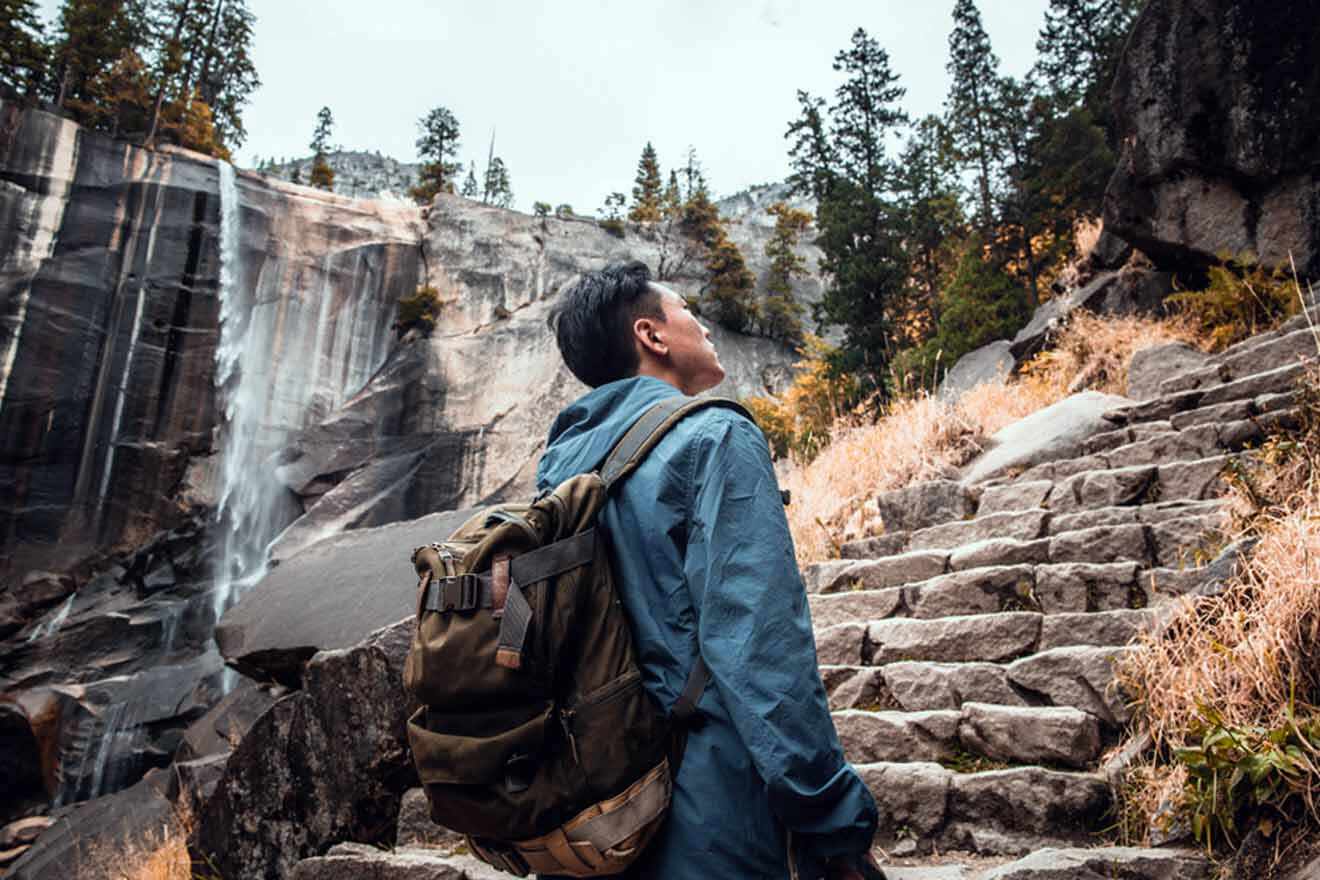 A man with a backpack standing next to a waterfall in yosemite national park.