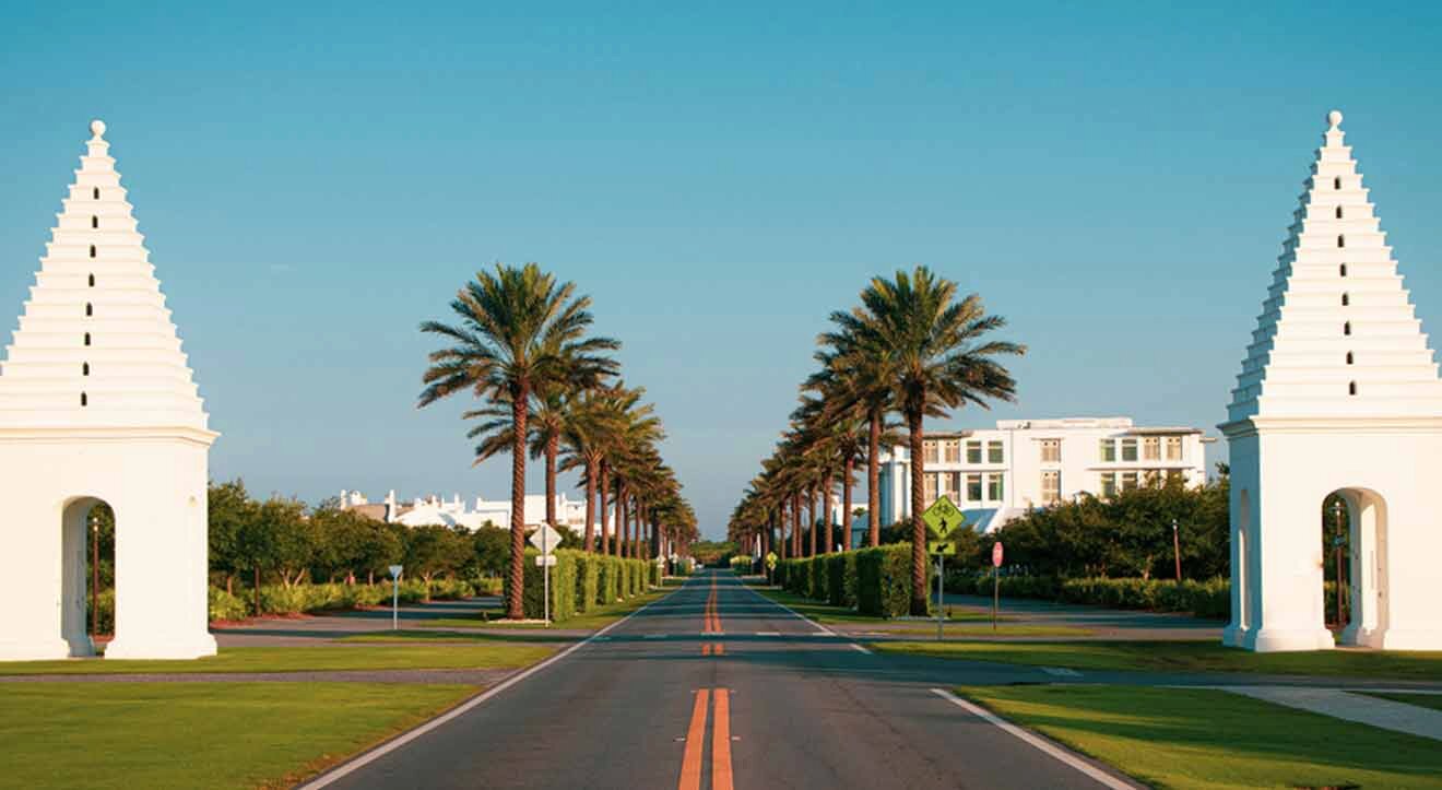 A white road with palm trees and white pillars.