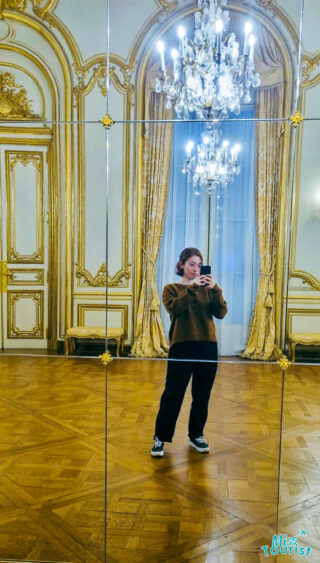 The writer of the post taking a selfie in a mirror within a lavishly decorated, gilded room, possibly within a historical building or museum in Buenos Aires, with intricate wall designs and a chandelier