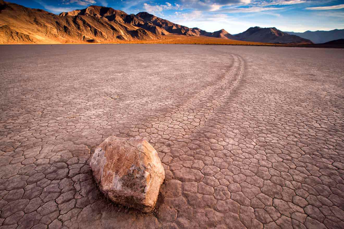 A rock in the middle of a desert with mountains in the background.