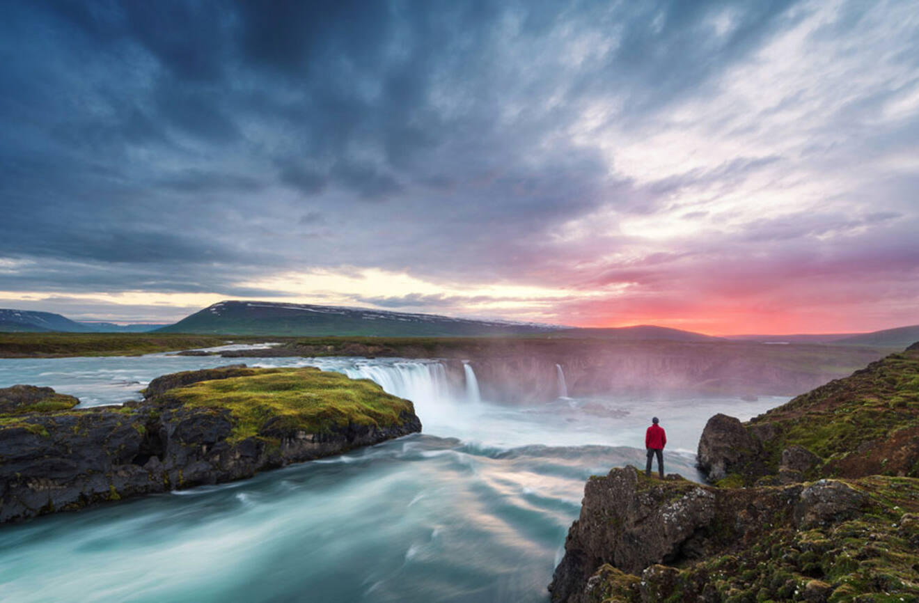 a person standing on top of a cliff overlooking a waterfall at sunset
