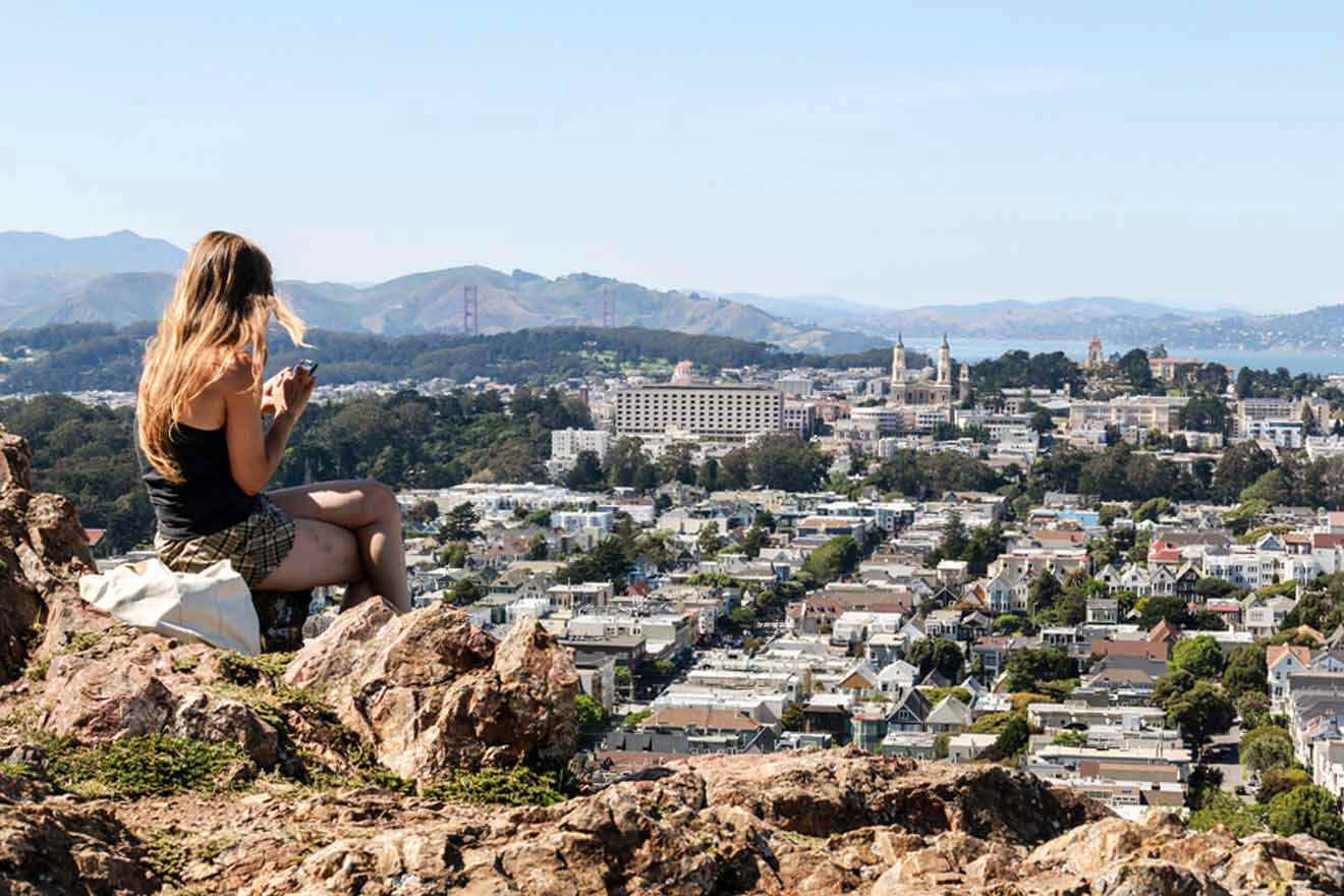 A woman sits on top of a hill overlooking the city of san francisco.