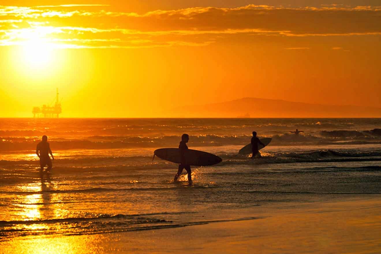A group of surfers walking on the beach at sunset.