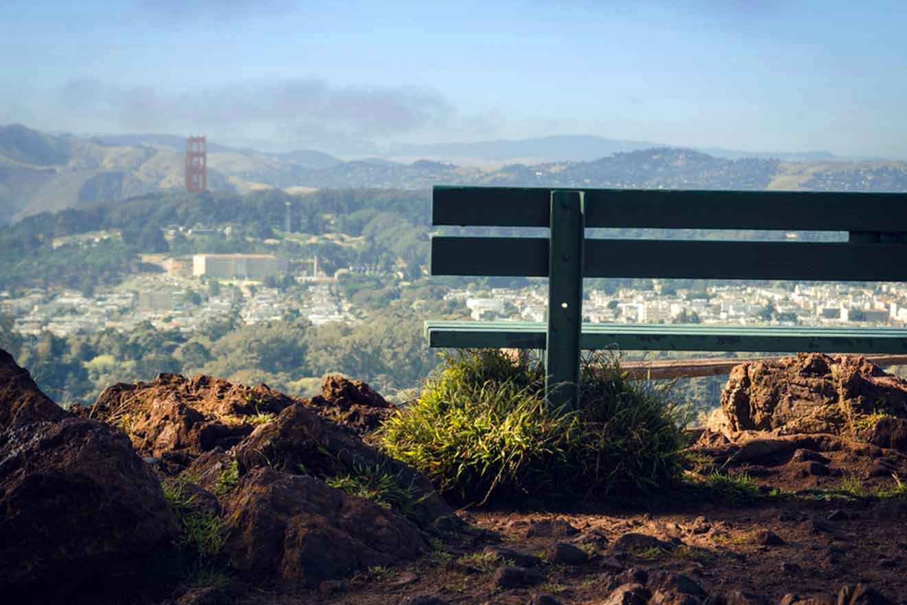 A green bench sits on top of a hill overlooking san francisco.