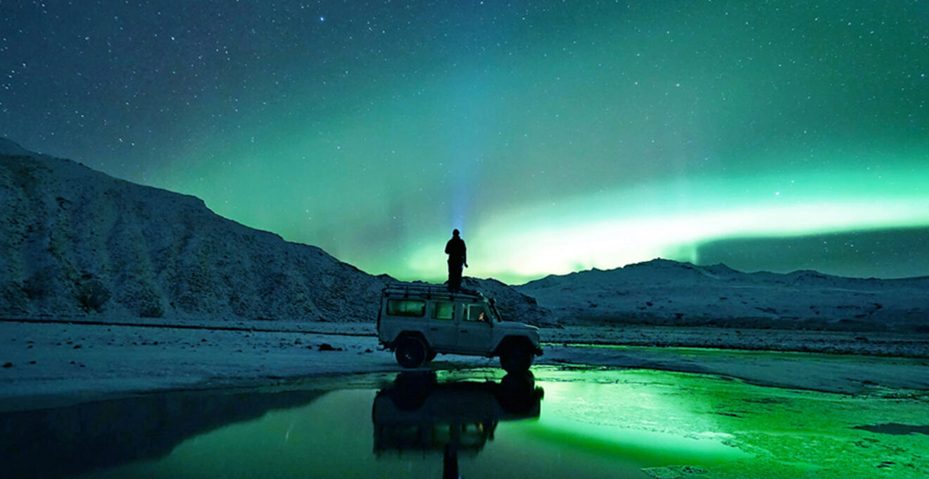 a eprson stading on top of a car looking at norther lights